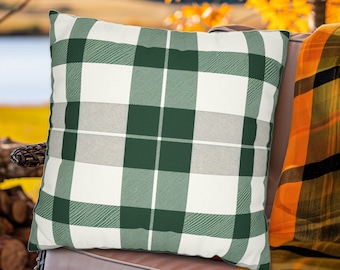 Op de afbeelding: Een groen en wit geruit kussen met een zachte, textuurrijke stof. Het kussen ligt op een bruine rieten stoel met een geel en zwart geruit plaid.