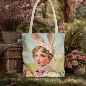 Op de afbeelding: Een canvas draagtas met een vintage illustratie van een persoon met konijnenoren en een roze strik. Het kunstwerk heeft een pastelkleurenpalet met een lentethema. De tas heeft crèmekleurige handvatten.