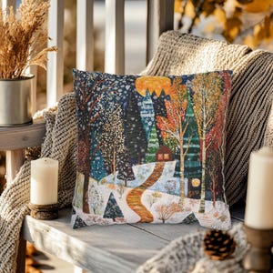 May include: A decorative cushion featuring a winter scene with a cabin in a snowy forest. The cushion has a colourful, whimsical design with a yellow moon and a winding path.