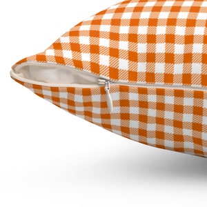Op de afbeelding: Een oranje en wit geruit kussen met een rits.