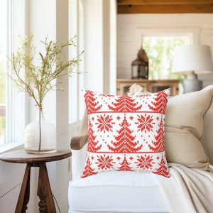 May include: Red and white throw pillow with a knitted Christmas tree and snowflake pattern. The pillow is on a white sofa with a white throw blanket.