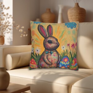 May include: Square decorative pillow with a colorful Easter bunny illustration. The artwork features a brown bunny with pink-lined ears, a blue bow tie, and colorful eggs in a field of flowers. The background is yellow with sun rays.