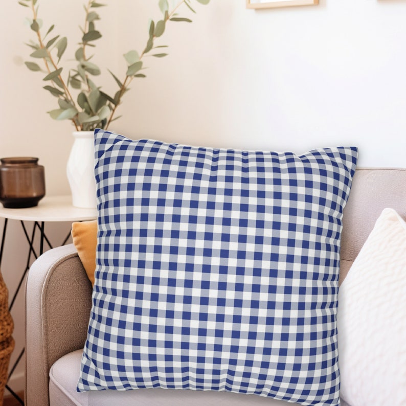 Puede incluir: Una almohada de tiro de gingham azul y blanco con un patr&oacute;n cuadrado. La almohada est&aacute; sentada en un sof&aacute; marr&oacute;n claro.
