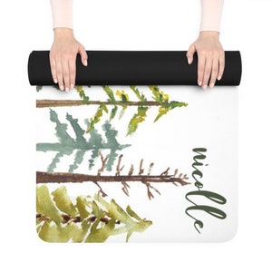 May include: A white yoga mat with a watercolor design of three green pine trees and the name "nicole" written in green script.