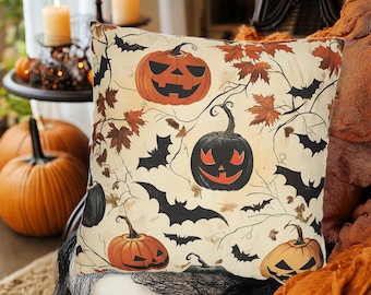 May include: Halloween-themed decorative pillow with a cream background featuring orange jack-o'-lanterns, black bats, and brown leaves. The pillow is square and sits on a white surface, with other Halloween decorations in the background.