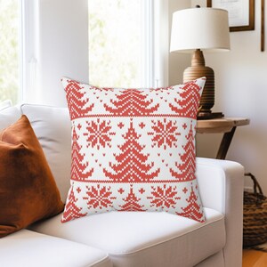 May include: Red and white throw pillow with a knitted Christmas tree pattern. The pillow is on a white sofa.