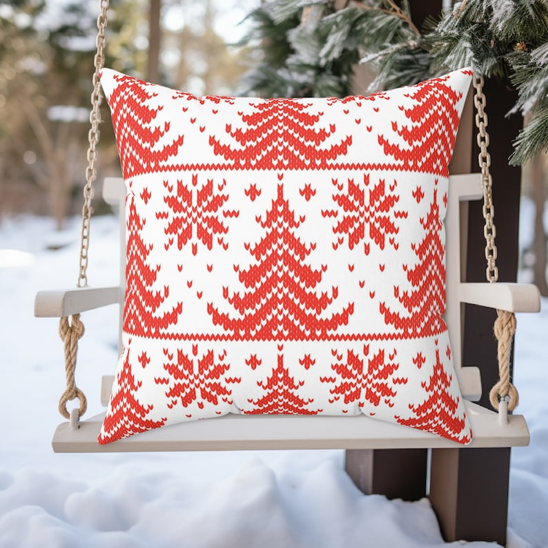 May include: Red and white knitted cushion with a Christmas tree pattern. The cushion is on a white wooden swing.
