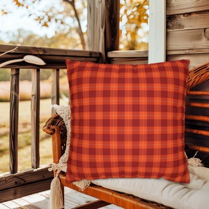 May include: A red and orange plaid throw pillow on a wicker chair on a porch.