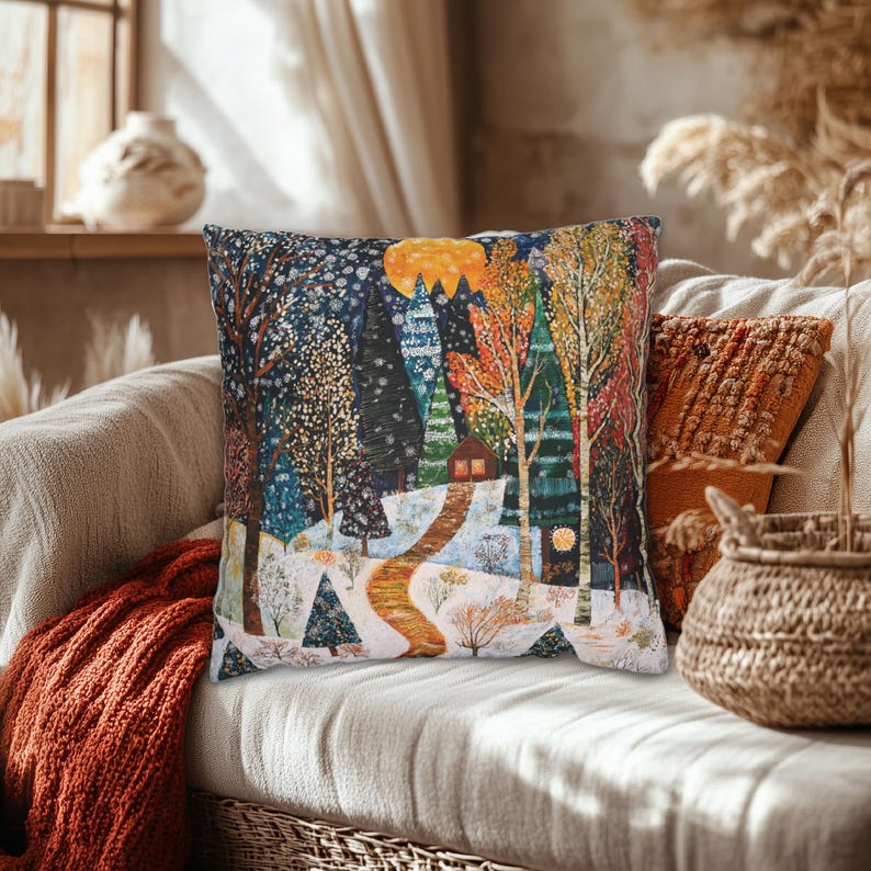 May include: A colourful throw pillow featuring a winter scene with a snowy path winding through a forest of trees and a small cabin in the distance. The pillow has a blue, green, yellow and orange colour scheme.