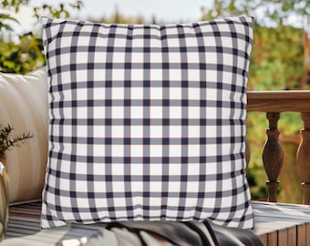 May include: A white pillow with a blue and red plaid pattern. The pillow is sitting on a wooden bench.