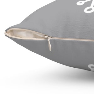 Puede incluir: Una almohada gris con cierre de cremallera blanco. La almohada tiene un dise&ntilde;o geom&eacute;trico blanco.