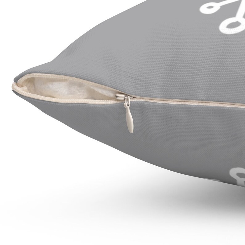 Puede incluir: Una almohada gris con cierre de cremallera blanco. La almohada tiene un dise&ntilde;o geom&eacute;trico blanco.
