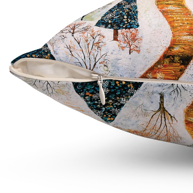 May include: A throw pillow with a zipper closure features a colourful abstract painting of trees and a winding path in a snowy landscape. The trees are painted in shades of blue, green, and yellow, while the path is a vibrant orange.