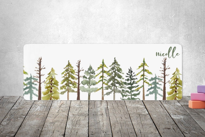 May include: A watercolor painting of a row of green pine trees with the name "nicolle" written in cursive at the top.