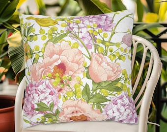 May include: A white throw pillow with a floral pattern featuring pink peonies, purple hydrangeas, and yellow birds. The pillow has a white background and is accented with green leaves.