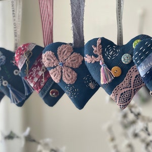 Puede incluir: Seis adornos de corazón de mezclilla hechos a mano con varios adornos, que incluyen bordados, encaje, botones y borlas. Los corazones están colgados de una cuerda y son de color azul claro.