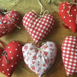 Könnte beinhalten: Sechs rote Stoffherzen mit verschiedenen Mustern, darunter Gingham, Punkte und Blumenmuster. Jedes Herz hat ein Schlüsselloch und einen Schlüsselanhänger. Die Herzen hängen an einer Schnur.