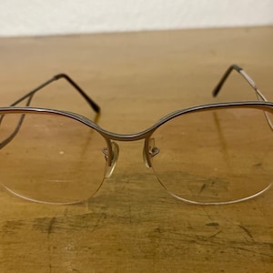 May include: Silver-toned eyeglasses with a unique, curved frame and clear lenses.