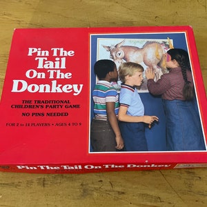 May include: A red box game for children called "Pin The Tail On The Donkey". The box features a picture of three children playing the game with a donkey on the wall. The text on the box says "The Traditional Children's Party Game. No Pins Needed. For 2 to 14 Players. Ages 4 to 9."