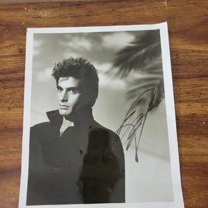 Puede incluir: Fotografía en blanco y negro de un hombre con una chaqueta oscura, con una firma en la esquina superior derecha. El hombre mira hacia la izquierda, con una palmera al fondo.