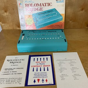 May include: A vintage "Rolomatic Bridge" game set, with a teal game board and box. The box reads "Set I for Beginners" and includes instruction booklets. The game is designed to help players learn the fundamentals of bridge.