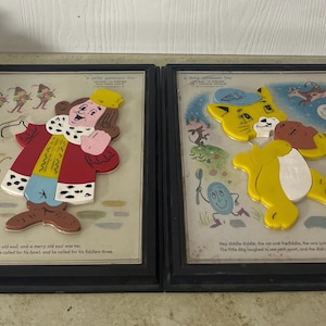 Può includere: Due illustrazioni vintage incorniciate di storie per bambini. Uno raffigura un re in un cappotto rosso, l'altro un gatto giallo. Ogni cornice ha un bordo nero e include il testo della storia.
