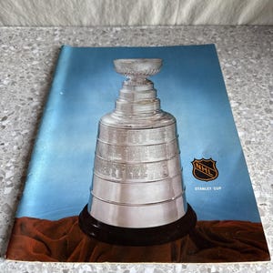 May include: A magazine featuring the Stanley Cup trophy, a silver cup with a black base, set against a blue and red background. The NHL logo and "STANLEY CUP" text are visible.