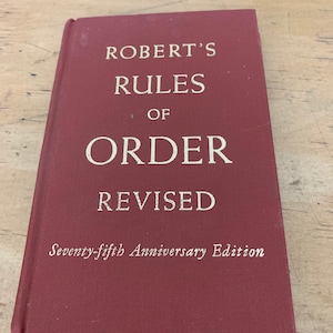 May include: A burgundy hardcover book titled "Robert's Rules of Order Revised" with the text "Seventy-fifth Anniversary Edition" printed on the front cover.
