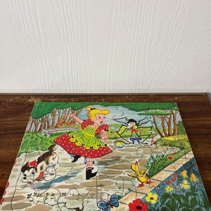 Può includere: Un puzzle vintage che presenta una ragazza con un vestito rosso e bianco, un cane, un'anatra, una farfalla e un ragno in una ragnatela. Il puzzle è ambientato in un giardino con fiori e alberi.