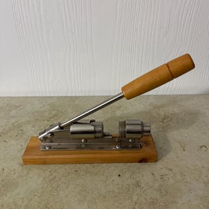 May include: A vintage nutcracker with a wooden handle and a metal cracking mechanism mounted on a wooden base.