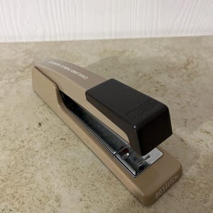 May include: A beige and brown Bostitch stapler with the text "Oakland Public Schools" and "Bostitch" printed on the side.