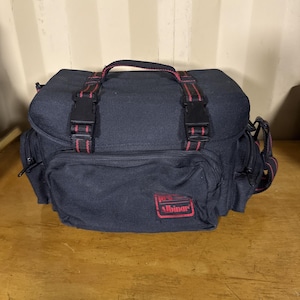 Può includere: Borsa per fotocamera nera con dettagli rossi. La borsa ha una maniglia superiore e cinghie regolabili con fibbie nere. La parte anteriore della borsa ha una tasca con cerniera e un logo rosso con la scritta "pro Albinar".