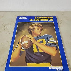 以下が含まれることがあります： 青と金のユニフォームを着たフットボール選手の肖像画が描かれた、ヴィンテージのフットボールゲームプログラムです。 プログラムのタイトルは「CALIFORNIA VS. SOUTHERN CAL」で、「THE JOE ROTH MEMORIAL GAME」と「touchdown illustrated」のテキストが含まれています。