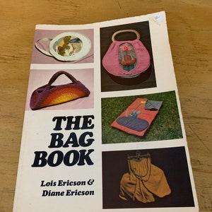 Può includere: Un libro vintage intitolato "The Bag Book" di Lois Ericson & Diane Ericson. La copertina presenta immagini di varie borse fatte a mano, tra cui una borsetta rosa con un design floreale e una borsa all'uncinetto con un gradiente arcobaleno.