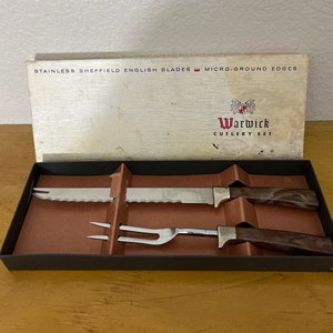 May include: Vintage Warwick Cutlery Set in a box. The set includes a carving knife, a carving fork, and a carving knife. The blades are stainless steel with micro-ground edges. The handles are brown with a marbled design.