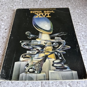 Può includere: Una copertina di programma vintage del Super Bowl XVI con il trofeo Vince Lombardi. La copertina ha uno sfondo nero con il logo del Super Bowl e il trofeo in argento, oro e blu. L'opera d'arte è stilizzata e dettagliata.