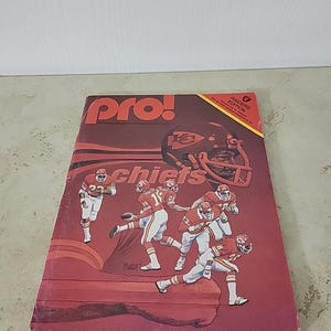May include: A vintage "Pro!" magazine cover featuring the Kansas City Chiefs football team. The cover is predominantly red with illustrations of players in action, a helmet, and the team name. The magazine is a Raiders Edition.