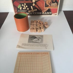 May include: Vintage Scrabble Sentence Cube Game. The game includes a box with a picture of people playing, a brown cup, wooden dice with letters, and game instructions. The game board is tan with a grid.