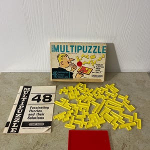 May include: A vintage MultiPuzzle game set. The box features a cartoon illustration of a man with puzzle pieces. Includes a booklet, yellow puzzle pieces, and a red tray. The box reads "48 Fascinating Puzzles Rolled Into".