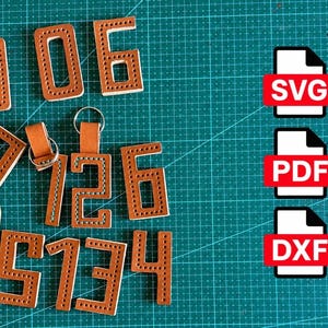 Op de afbeelding: Een verzameling van bruine lederen cijferuitsparingen met voorgeponste stikgaatjes langs de randen. Twee cijfers zijn voorzien van metalen sleutelringen. Drie witte bestandspictogrammen met rode labels tonen de tekst SVG, PDF en DXF.