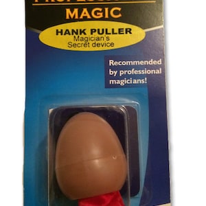 May include: A magic trick kit labeled "PROFESSIONAL MAGIC" with a brown egg-shaped device and a red cloth. The packaging includes the text "HANK PULLER Magician's Secret device" and "Recommended by professional magicians!"