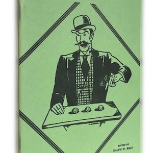 May include: A green booklet with a black and white illustration of a man in a top hat and suit performing the shell game. The title of the booklet is "The Three Shell Game" and the text "Edited by Ralph W. Read" is at the bottom.