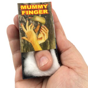 May include: A small, black box with a white cotton finger inside. The box has a label that says "MUMMY FINGER" in red and yellow letters.