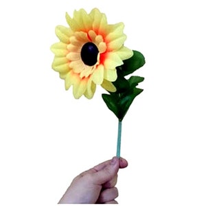 May include: A single artificial yellow and orange daisy flower with a dark brown center. The flower is attached to a green stem with leaves.