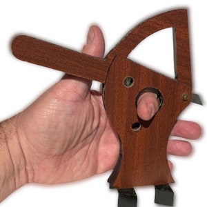 May include: A wooden finger trap toy with a brown finish. The toy has a handle and a small opening for a finger to be inserted. The toy is designed to trap the finger when the handle is pulled.