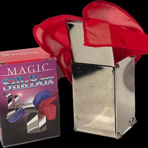 May include: A silver metal magic box with a red silk scarf on top. The box is labeled "Magic Silk Box" on the front.