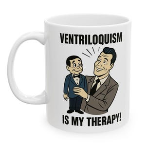 May include: White ceramic mug featuring a cartoon illustration of a man holding a ventriloquist dummy. The mug has the text "VENTRILOQUISM IS MY THERAPY!" in black, bold font. The illustration is in a vintage comic book style.