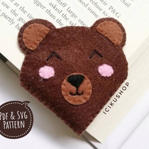 Könnte beinhalten: Ein braunes Filz-Bären-Lesezeichen mit rosa Wangen und einer braunen Nase. Das Lesezeichen ist herzförmig und trägt den Text "PDF & SVG PATTERN" und "ICIKUSHOP".