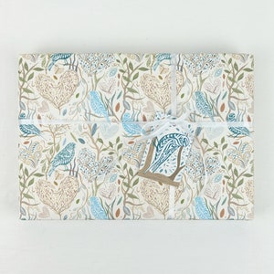 May include: White gift wrap with a blue and brown bird and leaf pattern. The gift is tied with a white ribbon and a blue and brown bird tag.