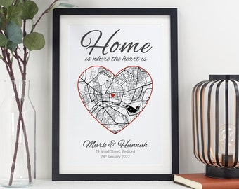 May include: A black framed print with the text "Home is where the heart is" and a heart-shaped map with a red dot in the center. The text "Mark & Hannah" is below the map, followed by an address and date.